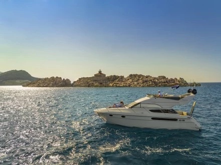 Fairline Phantom 40 at anchor off a rocky islet lighthouse in late-afternoon light, guests out on deck