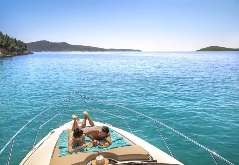 Two guests sunbathing on the bow pad of the Fairline Phantom 40 over a calm turquoise bay, islands on the horizon