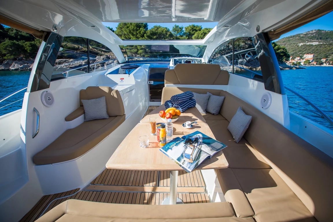 Cockpit of the Jeanneau Leader 10 — U-shaped tan seating and teak table set with fruit under the open sunroof