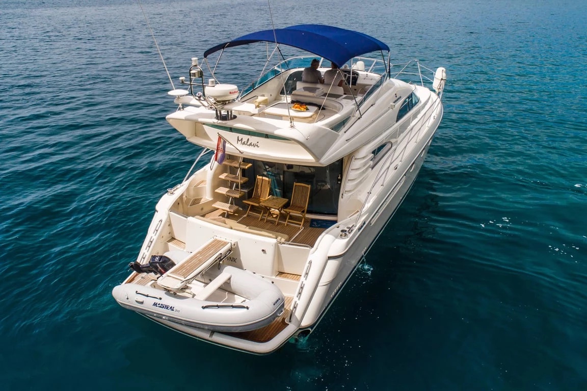 Stern view of the Malavi 55 at anchor showing the flybridge dining area, teak cockpit and tender