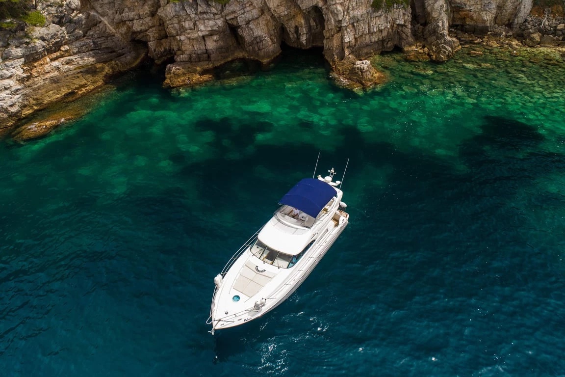 Aerial view of the Malavi 55 moored over emerald shallows in a cliff-lined cove
